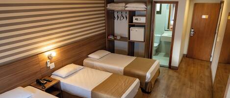A hotel room with two beds, a wooden wardrobe, a small kitchenette, and a bathroom visible through an open door.