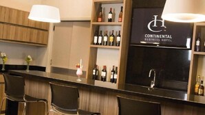 Eine Bar mit zahlreichen Weinflaschen, einem schwarzen Schild mit der Aufschrift "Continental Business Hotel" und zwei Pendelleuchten.