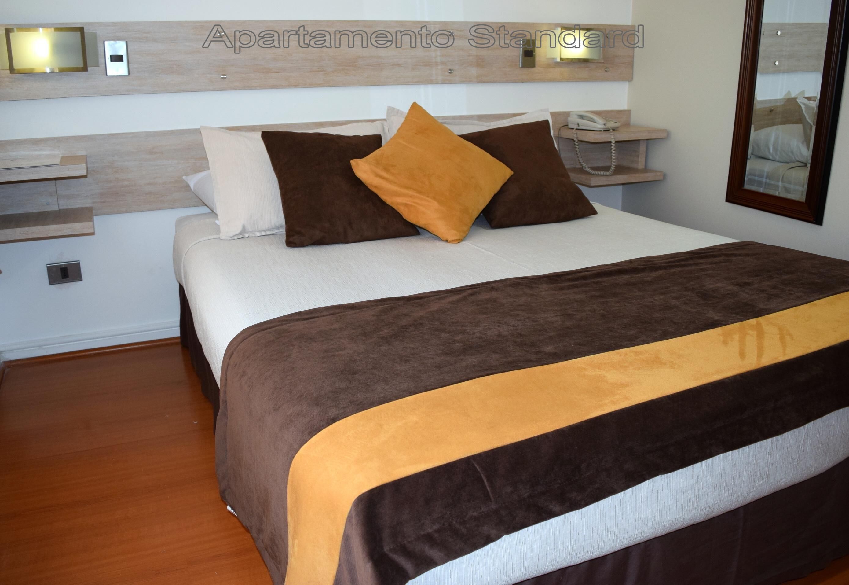 Un dormitorio ordenado con cama, almohadas, mesitas de noche y un espejo.