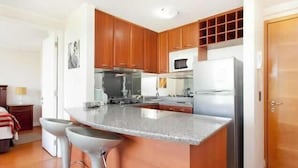 A modern kitchen with wooden cabinets, a central island, and bar stools. - Apart Hotel Cambiaso (Santiago)