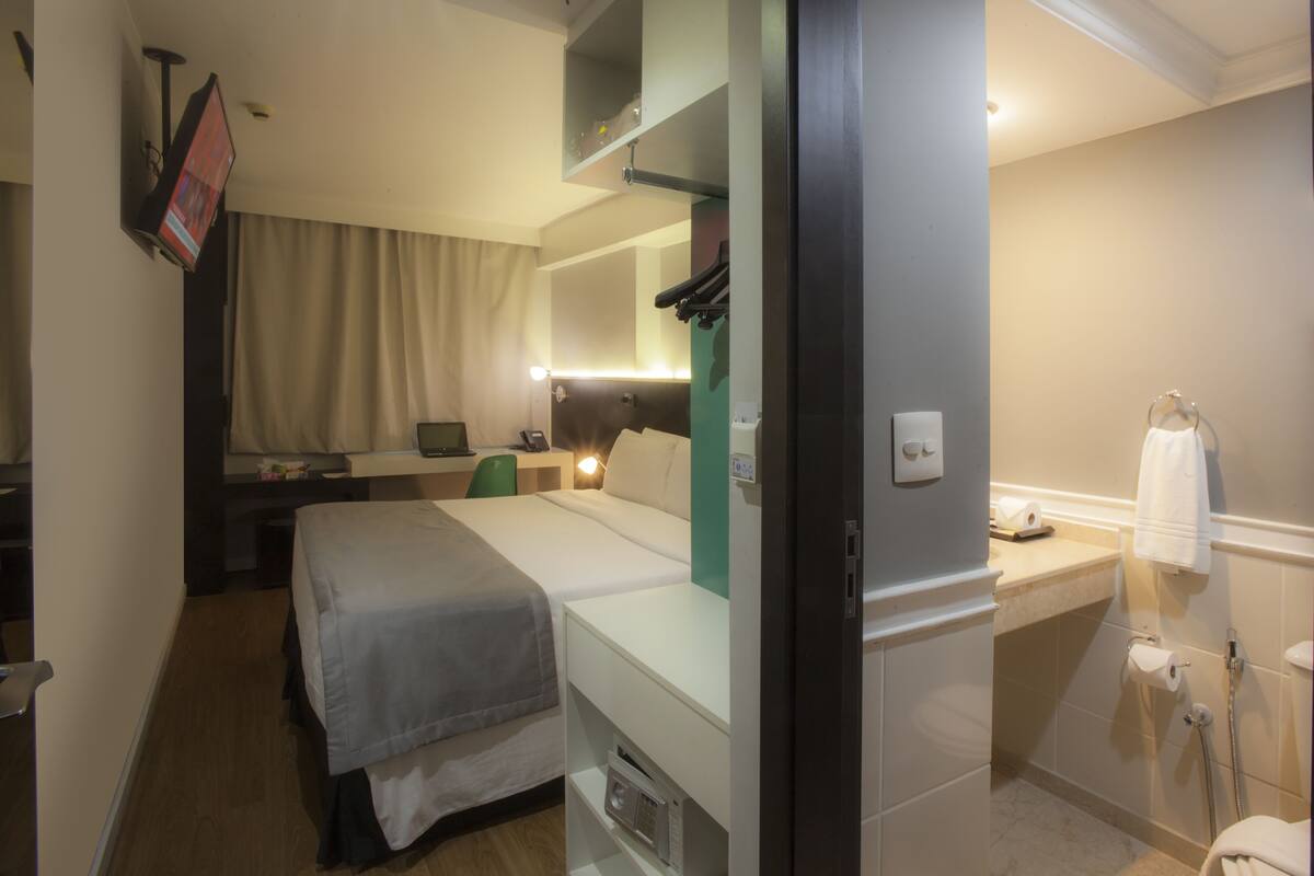 Une chambre d’hôtel comprenant un lit, une table de chevet, un bureau, une chaise et une salle de bain avec un lavabo et un porte-serviettes.