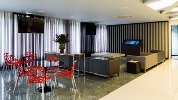 A modern hotel lobby with a reception desk, seating area, and a large flat-screen TV.
