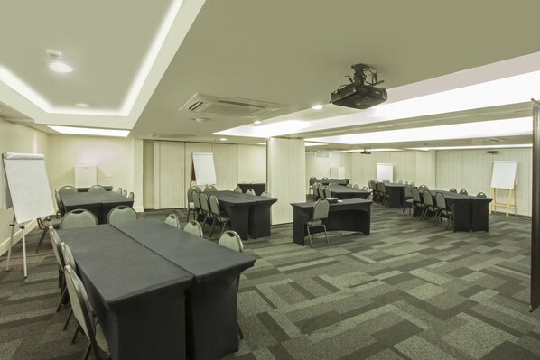 A conference room with multiple tables and chairs, whiteboards, and a projector on the ceiling.