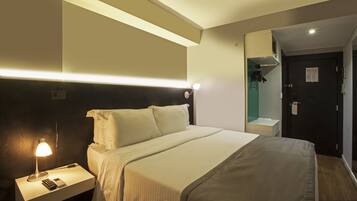 Una habitación de hotel con cama, mesita de noche, lámpara y espejo.