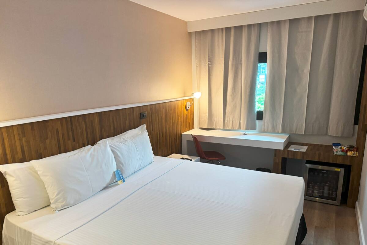 Une chambre d’hôtel avec un grand lit, un bureau, une chaise, une lampe et une vue sur l’extérieur.