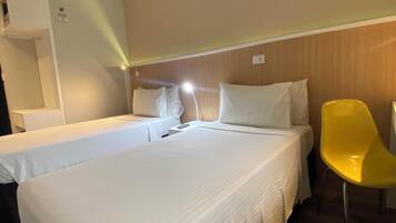 A hotel room with two single beds, a yellow chair, and a nightstand with a lamp.