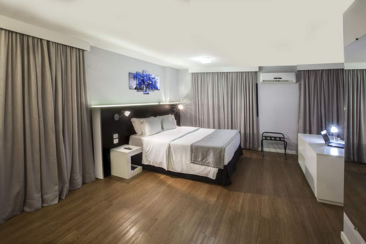 Une chambre d’hôtel moderne dotée d’un grand lit, de tables de chevet, d’un bureau avec un ordinateur portable et d’un appareil de climatisation.
