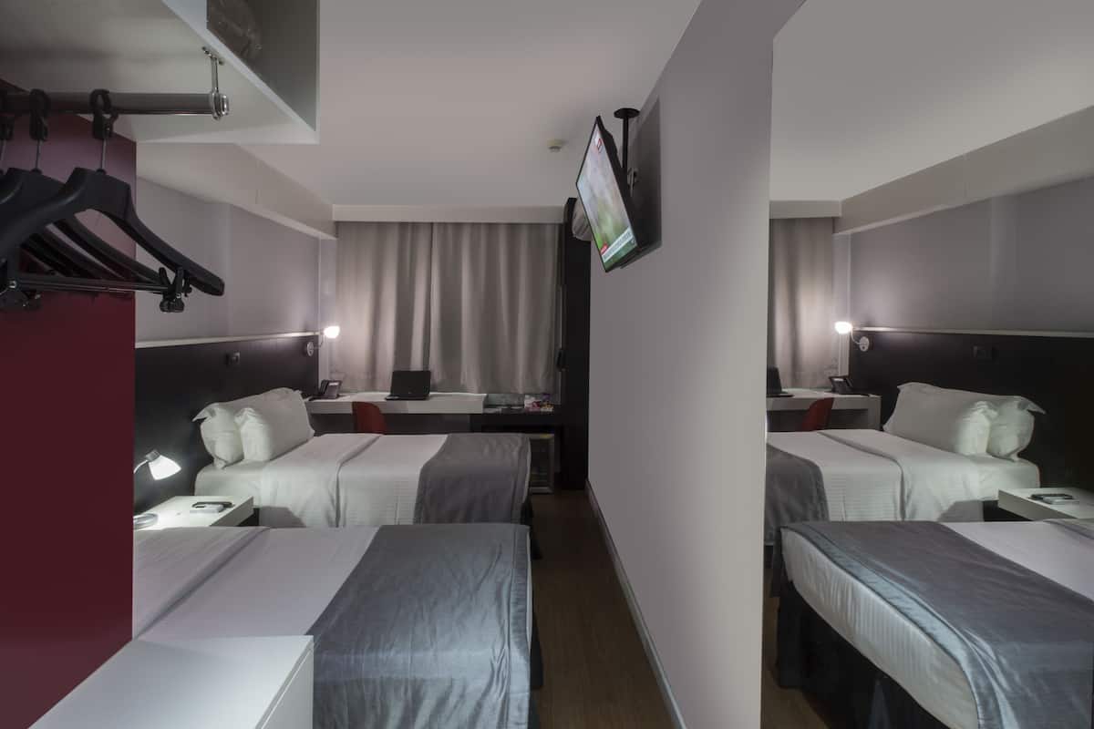 Une chambre d’hôtel avec deux lits, un bureau avec un ordinateur, un téléviseur fixé au mur et un porte-manteau.