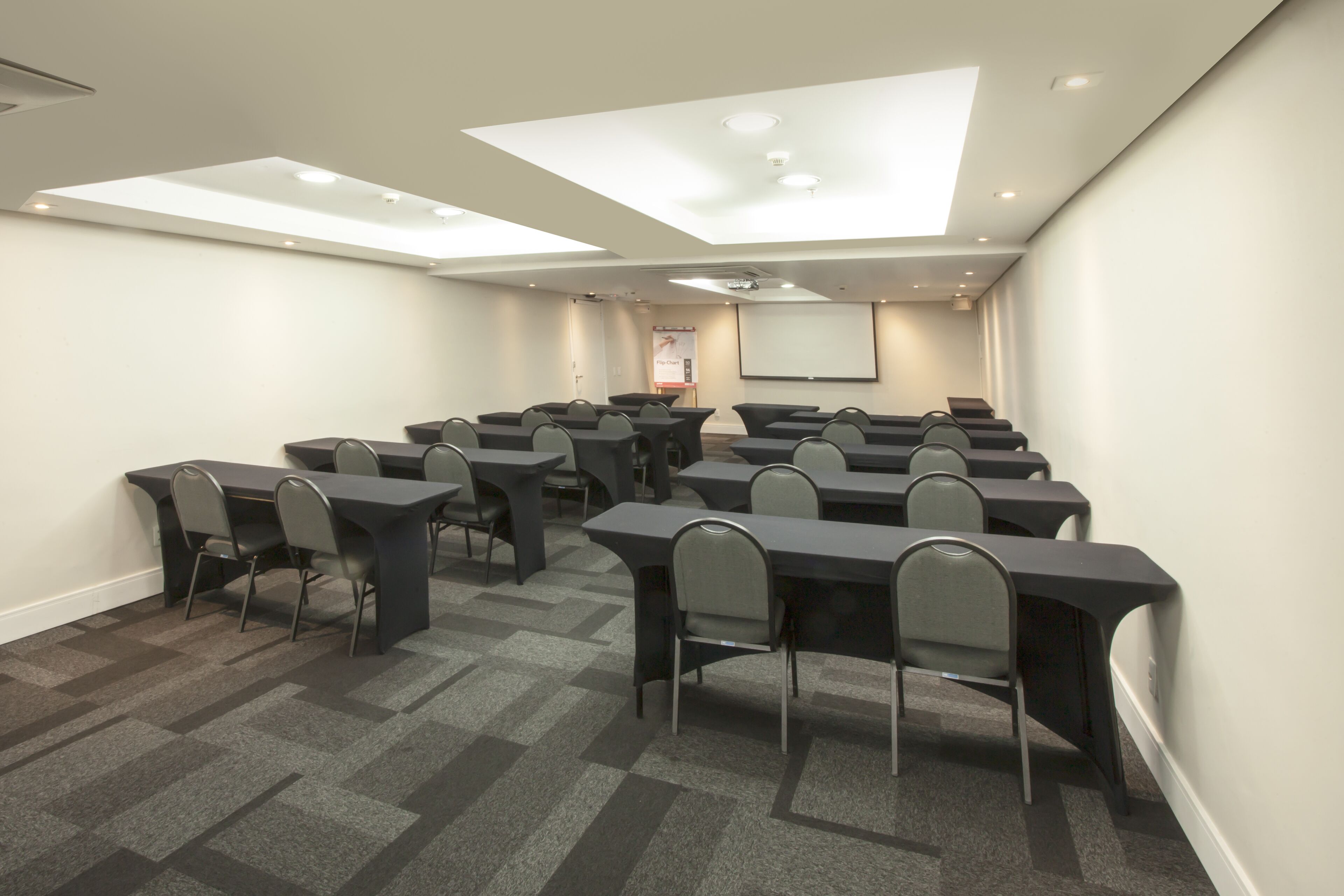 Uma sala de conferências com várias mesas e cadeiras, uma tela de projetor e uma tela de apresentação.