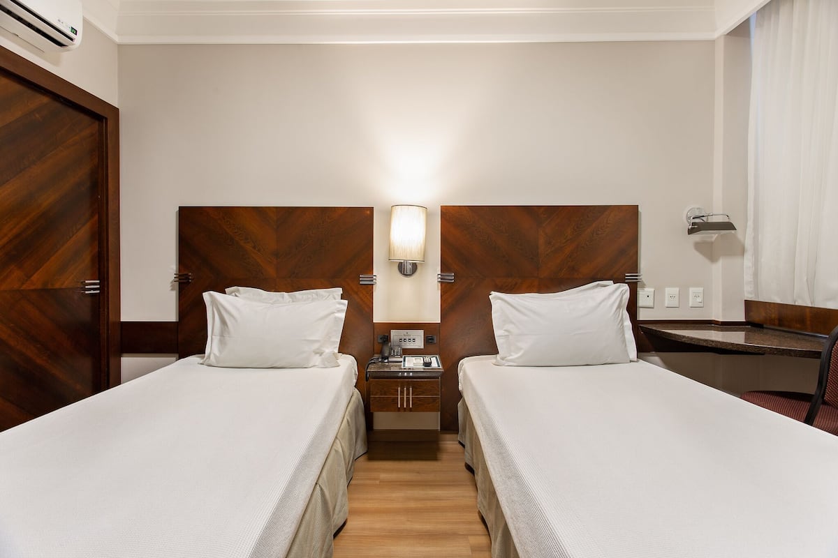 A hotel room with two beds, a desk, a nightstand, and a mirror.