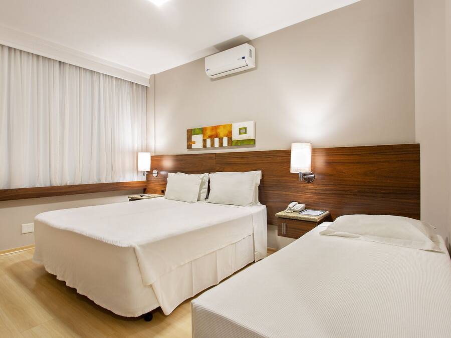 Hotelkamer met twee bedden, een houten hoofdbord, een nachtkastje met een lamp en een wandairco.