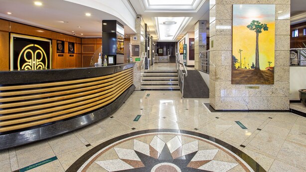 Zona de recepción de hotel con un mostrador curvo, una escalera y un cuadro grande en la pared.