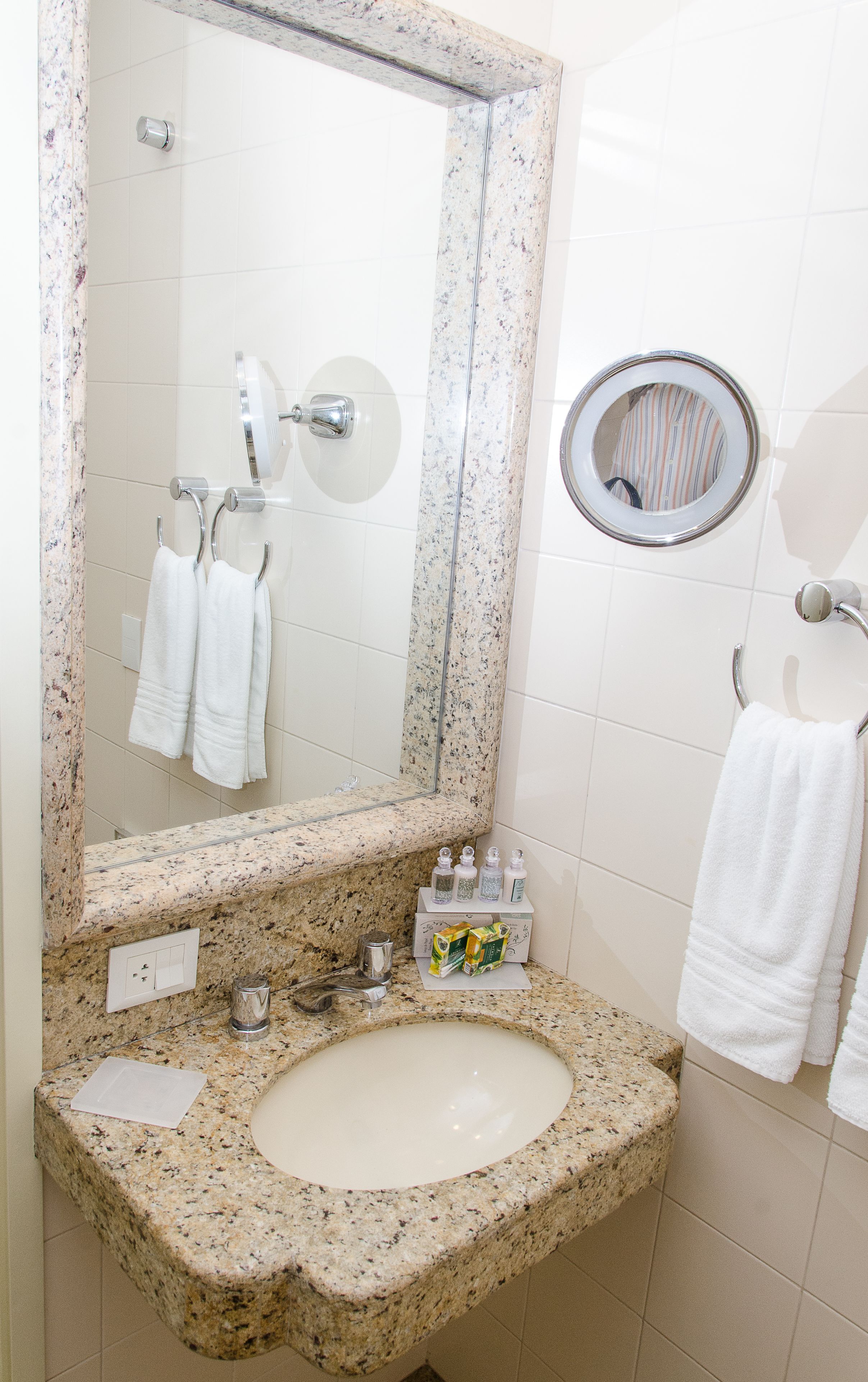 A bathroom with a granite countertop sink, a large mirror, a round mirror, and a towel rack.