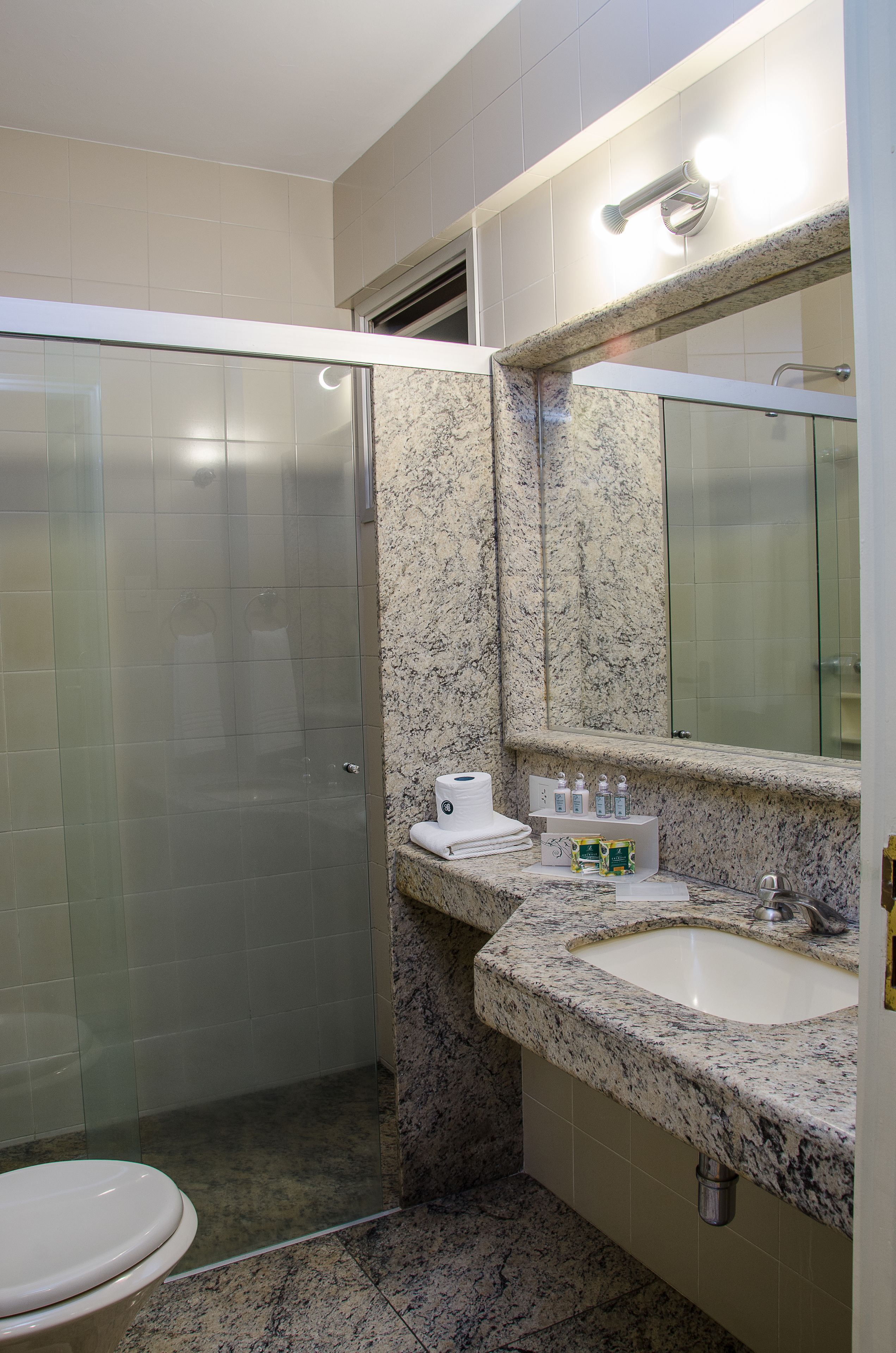 A bathroom with a glass shower enclosure, a sink with a granite countertop, and a mirror above the sink.