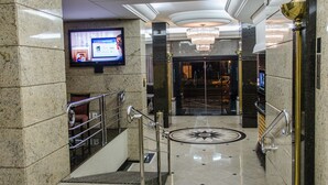 Un vestíbulo con piso de mármol, una escalera, una araña y una pantalla de televisión.