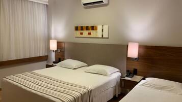 Quarto de hotel com uma cama grande, luminárias de cabeceira, telefone e ar condicionado na parede.