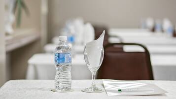 Una mesa con una botella de agua, un vaso con una servilleta y un bolígrafo sobre un mantel blanco.