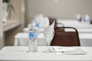 Una mesa con una botella de agua, un vaso con una servilleta y un bolígrafo sobre un mantel blanco.