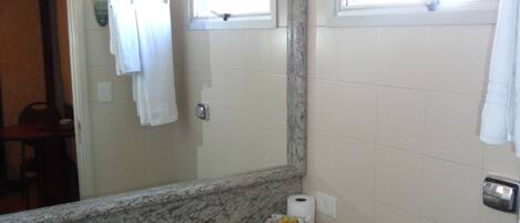 A bathroom with a granite countertop sink, a mirror, a towel rack, a window, and a shower.
