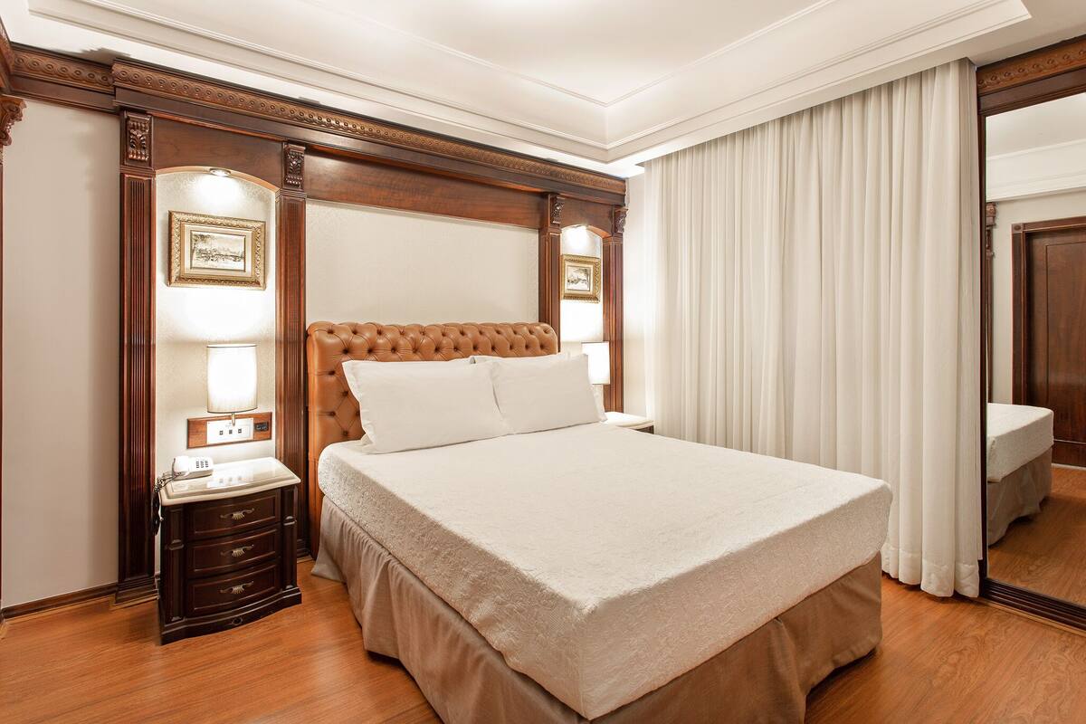 A large bed with a wooden headboard, a nightstand with a lamp, and a mirror on the wall.
