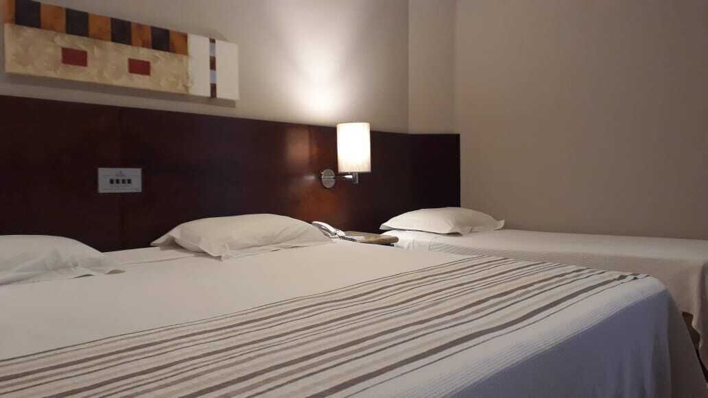 Una habitación de hotel con dos camas individuales, cabecera con lámpara y toma de corriente en la pared.