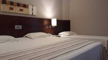 Una habitación de hotel con dos camas individuales, cabecera con lámpara y toma de corriente en la pared.