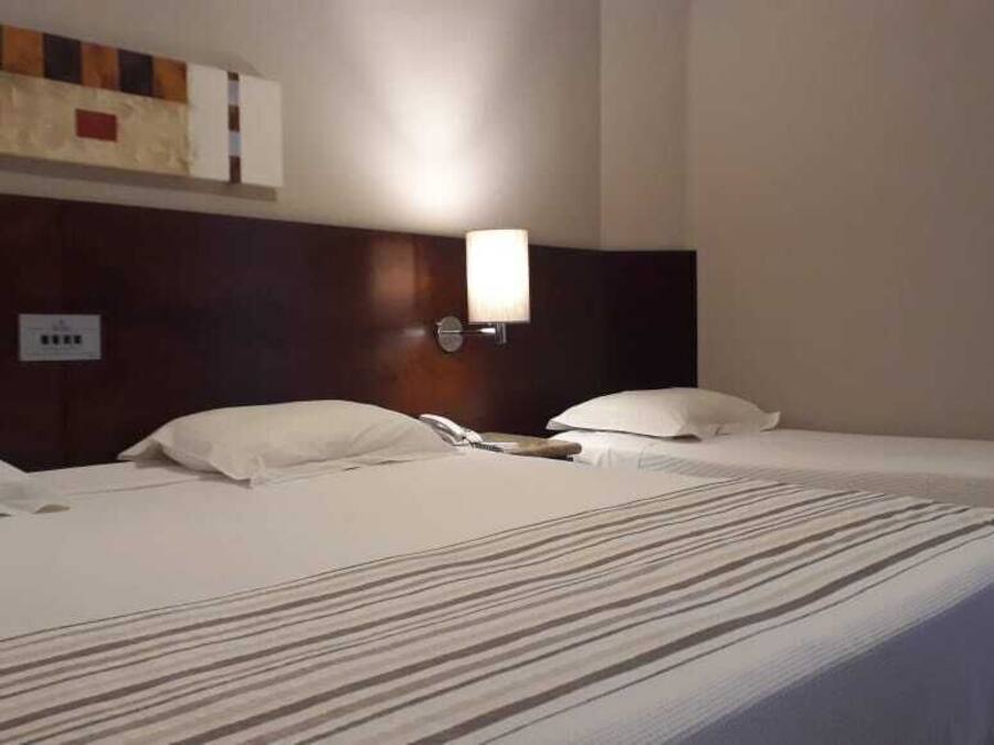 Una habitación de hotel con dos camas individuales, cabecera con lámpara y toma de corriente en la pared.