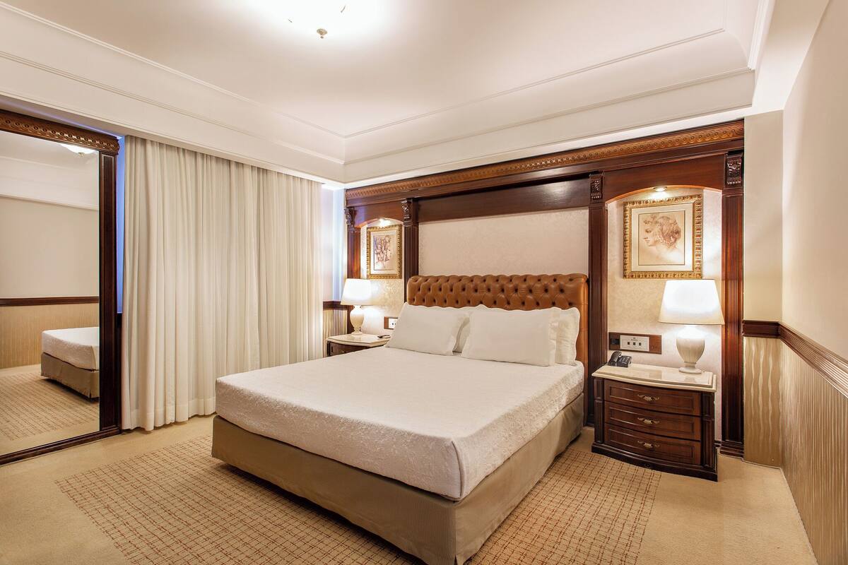 A hotel room with a large bed, a nightstand with a lamp, a dresser, and a mirror.