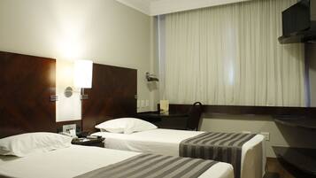 A hotel room with two beds, a desk, a chair, a TV, and a window with curtains.