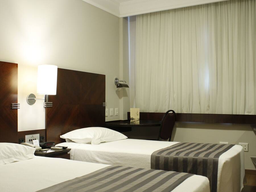 A hotel room with two beds, a desk, a chair, a TV, and a window with curtains.