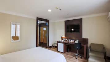 Quarto de hotel com cama, escrivaninha, cadeira e uma pequena cozinha.