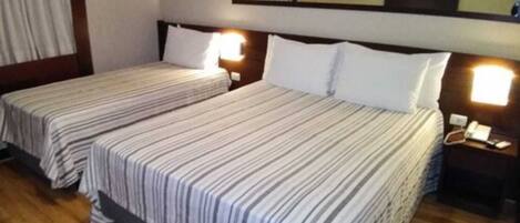 Una habitación de hotel con dos camas individuales, suelo de madera y lámparas de noche.