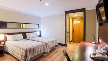 Una habitación de hotel con cama, mesita de noche, escritorio, silla y puerta que da a otra habitación.