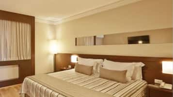 Een hotelkamer met een groot bed, twee nachtkastjes met lampen, een houten hoofdbord en een groot raam met gordijnen.