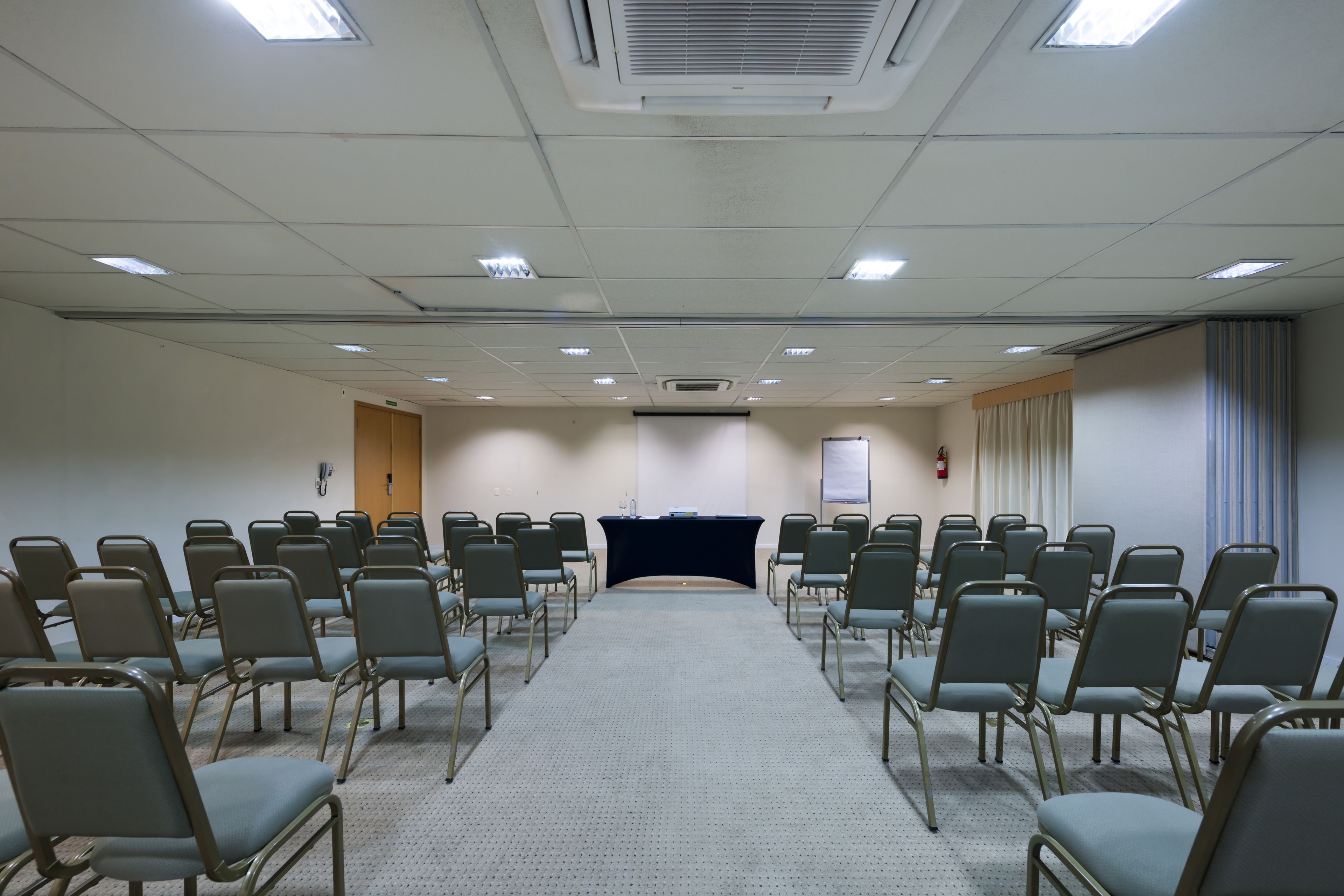 Une salle de conférence avec des rangées de chaises disposées face à une scène, un écran de projection et un pupitre.