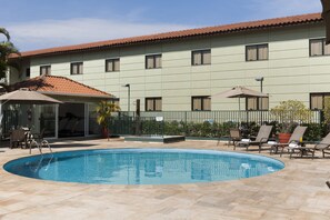 A swimming pool with lounge chairs and umbrellas, surrounded by a building with a tiled roof and multiple windows. - Hotel Matiz Jaguariúna (Jaguariuna)