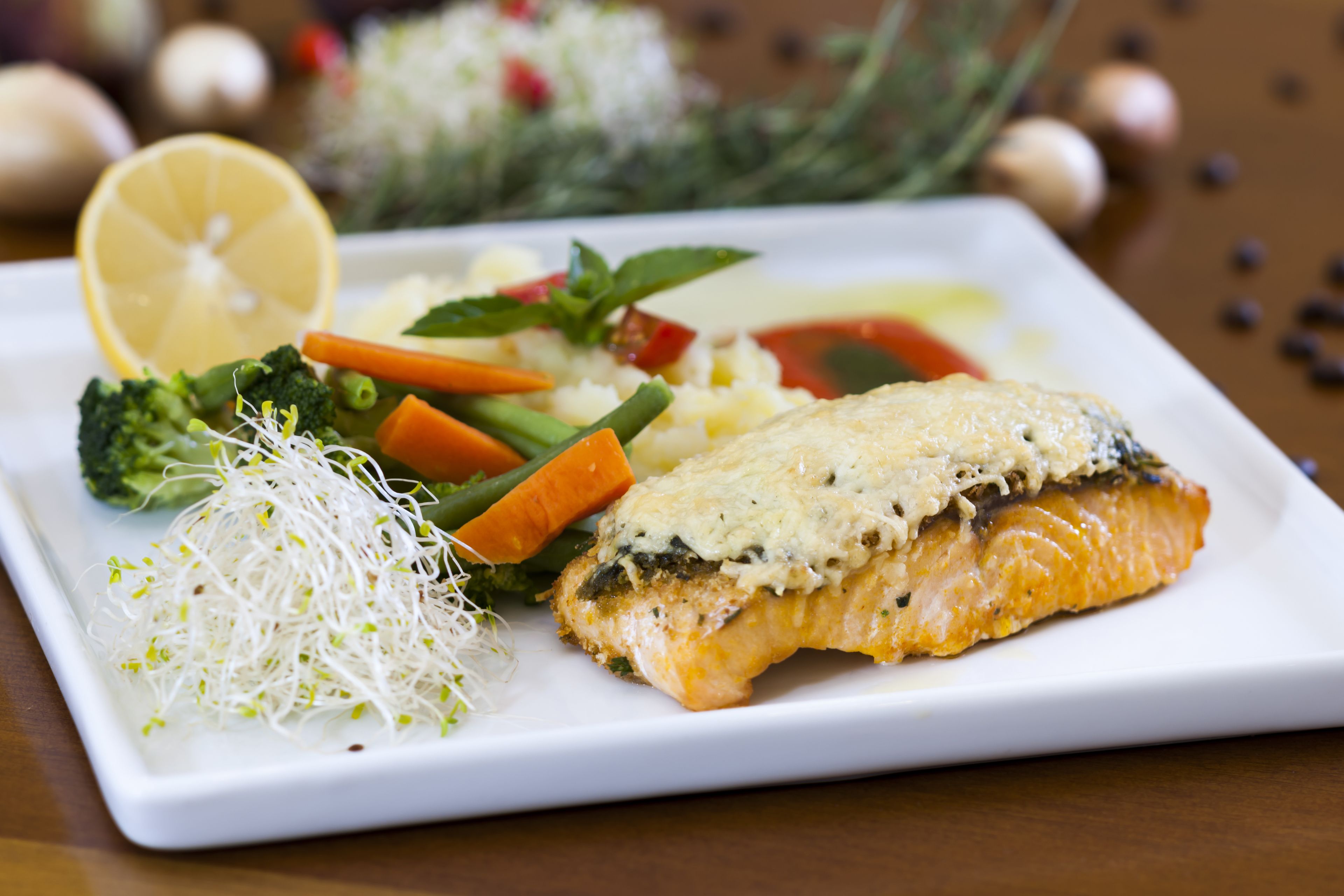 A plate of food with salmon, vegetables, and a lemon slice.