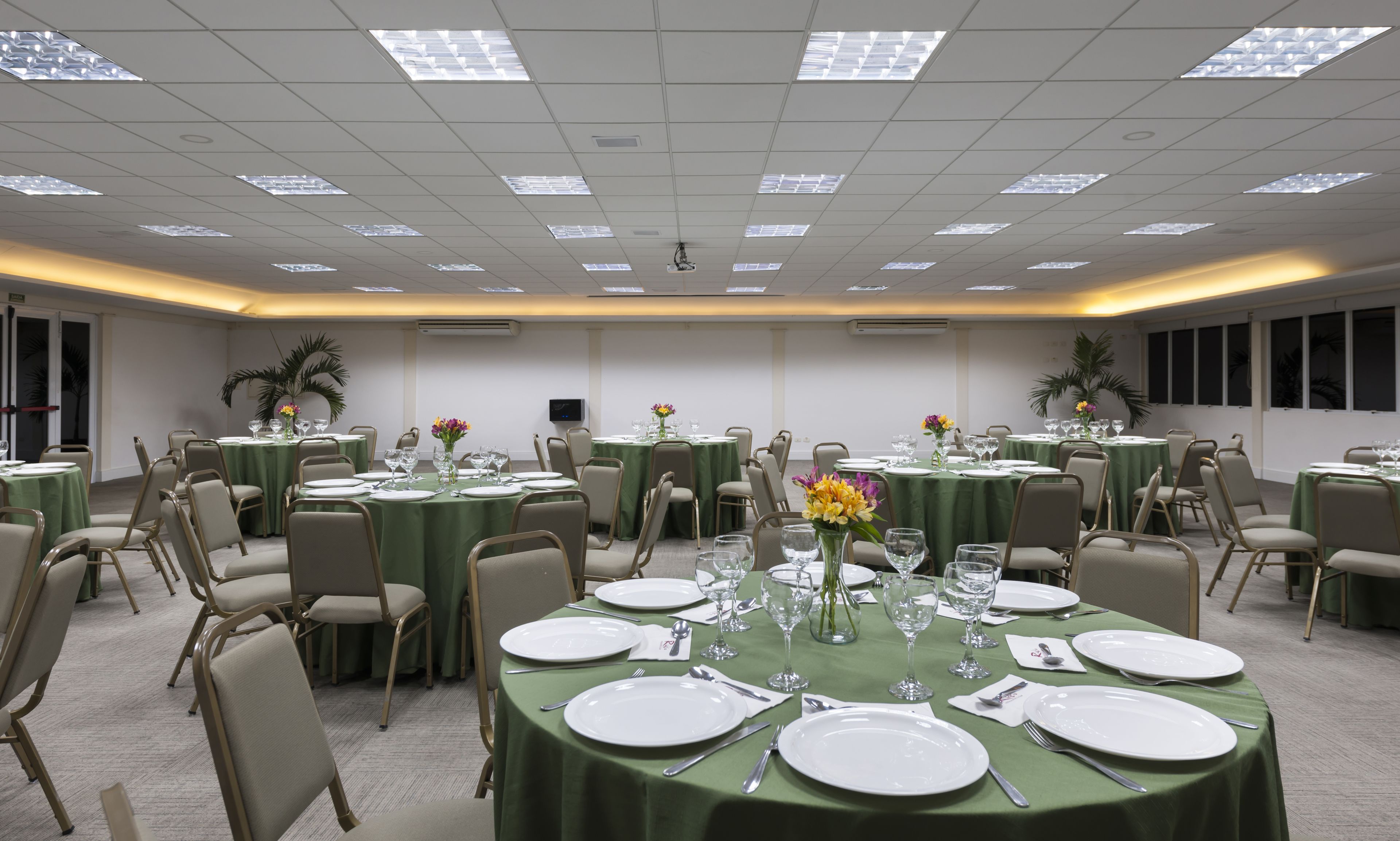 A conference room with multiple tables set for dining, equipped with chairs, plates, cutlery, and glassware.