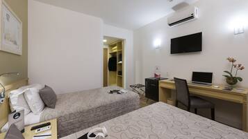 A hotel room with two beds, a desk with a laptop, a TV, and a small plant.