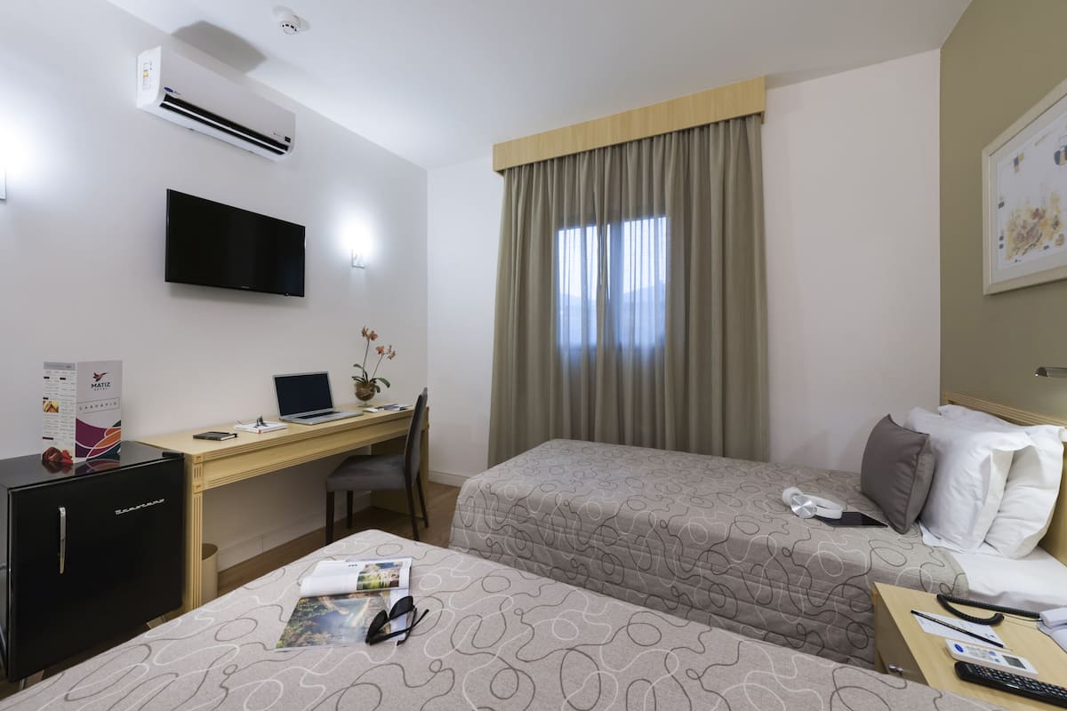 A hotel room with a desk, two beds, a TV, and a minibar.