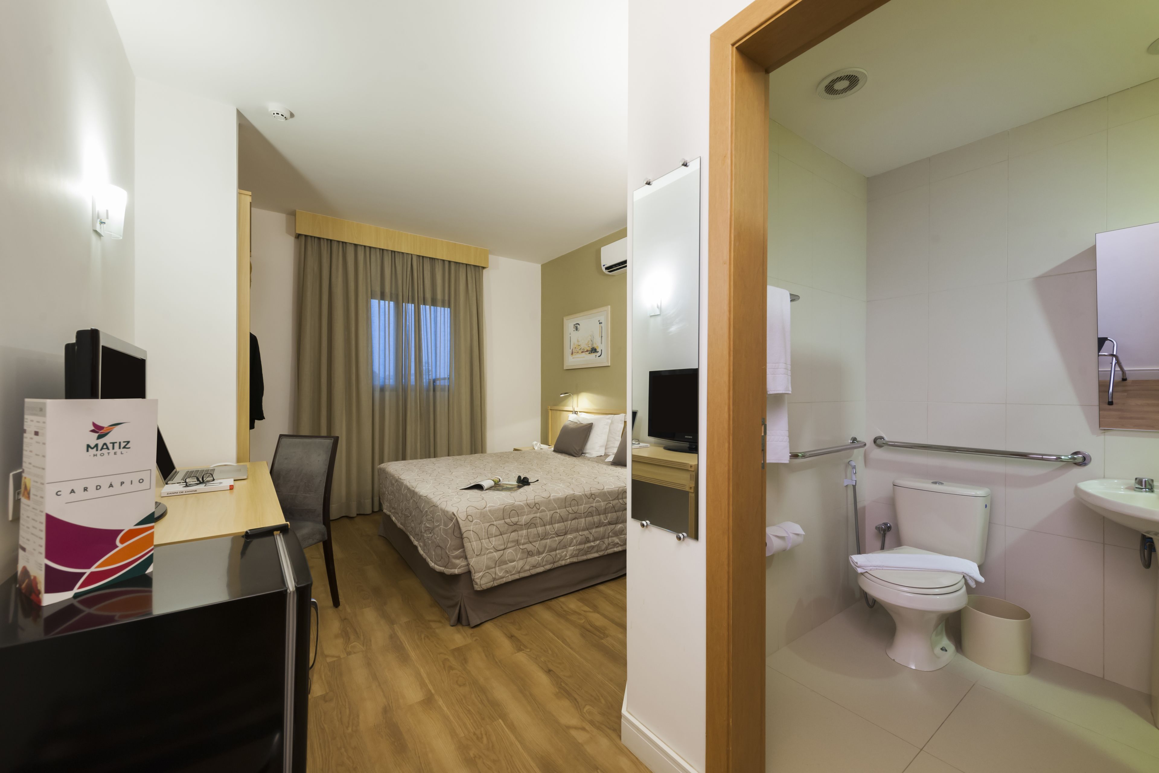 A hotel room with a bed, desk, chair, television, and a bathroom with a toilet and sink.