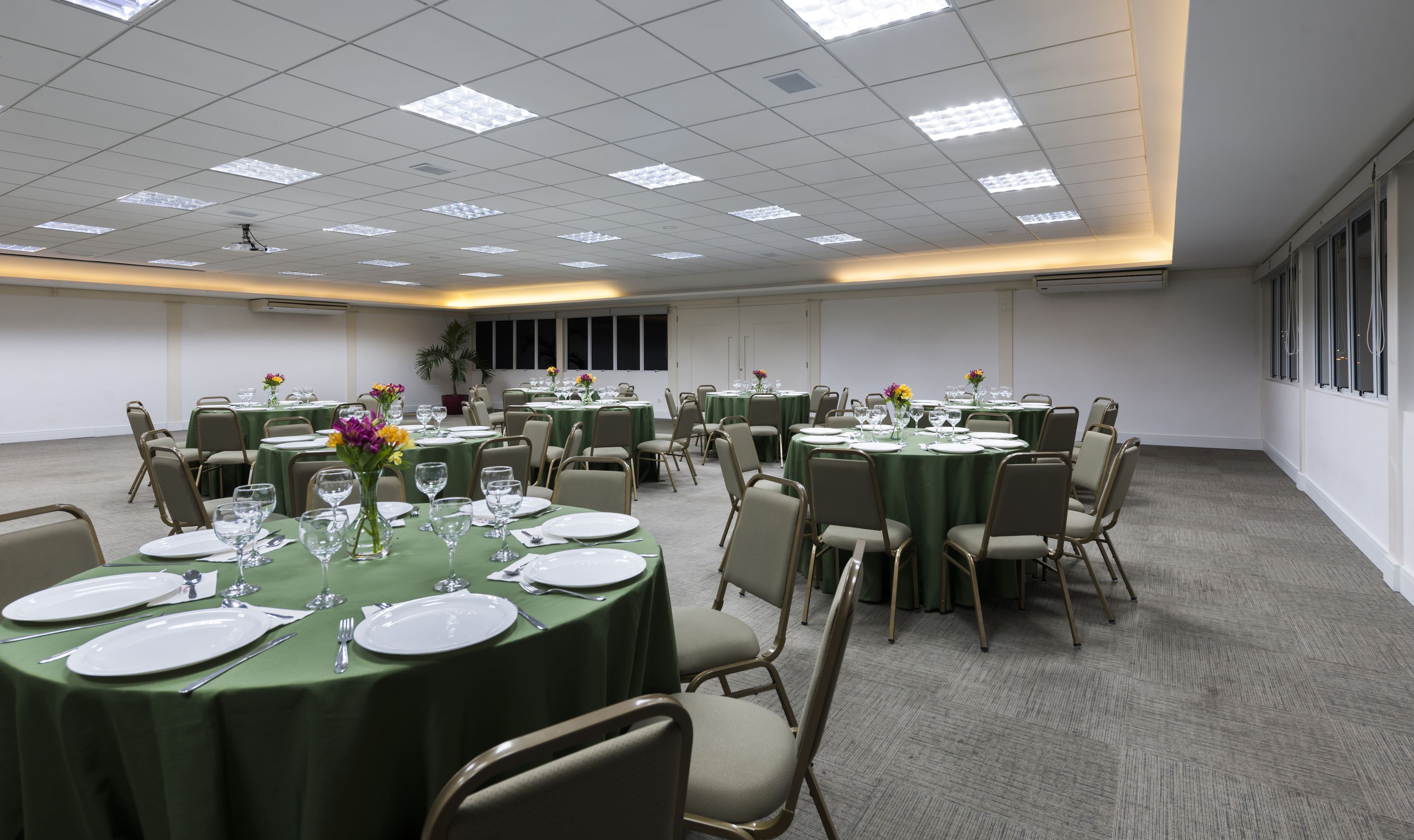 Un salón de conferencias con varias mesas dispuestas para comer, equipado con sillas y mesas cubiertas con manteles verdes.