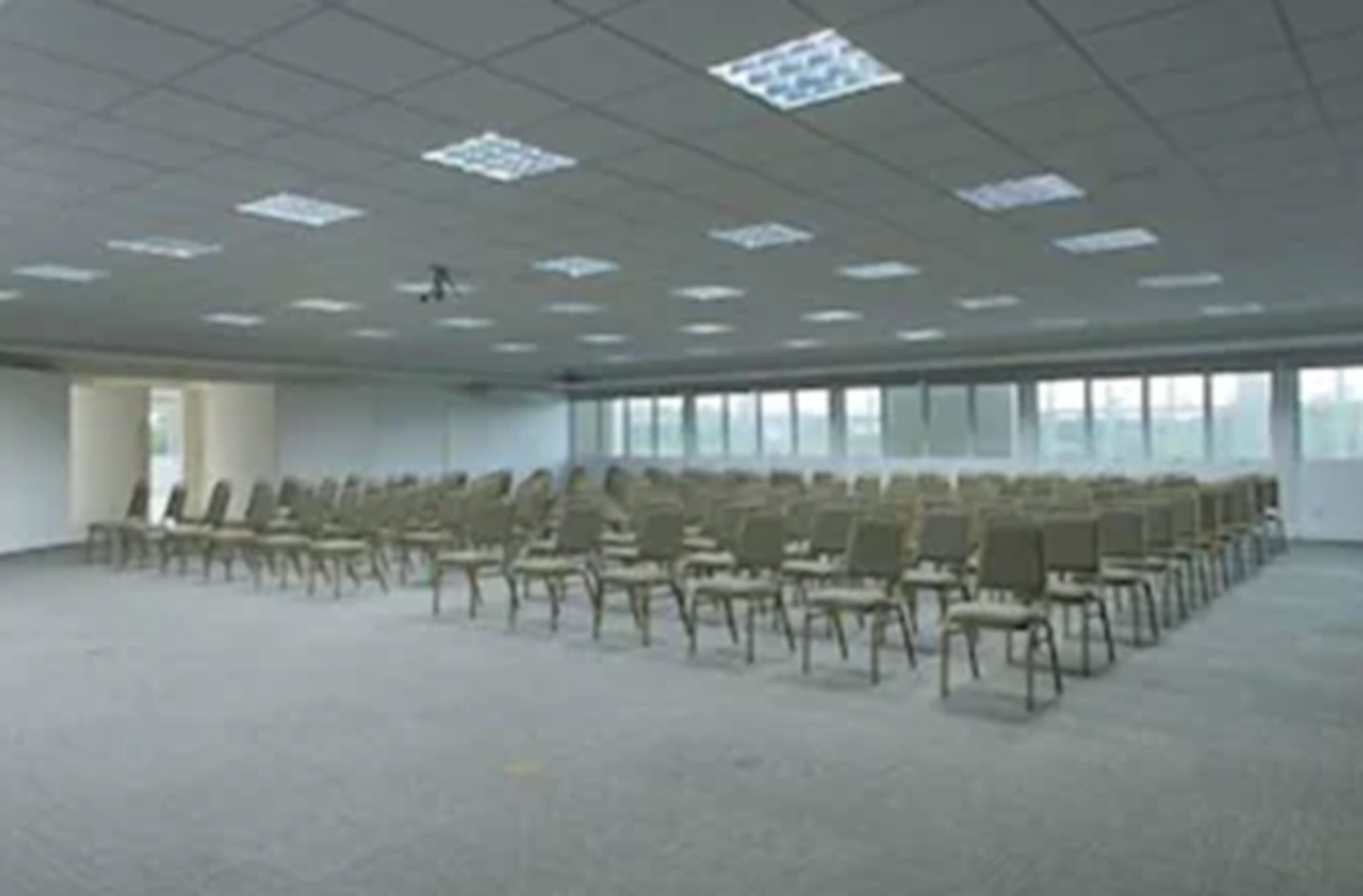 A large, empty conference room with rows of chairs and a high ceiling with fluorescent lighting.