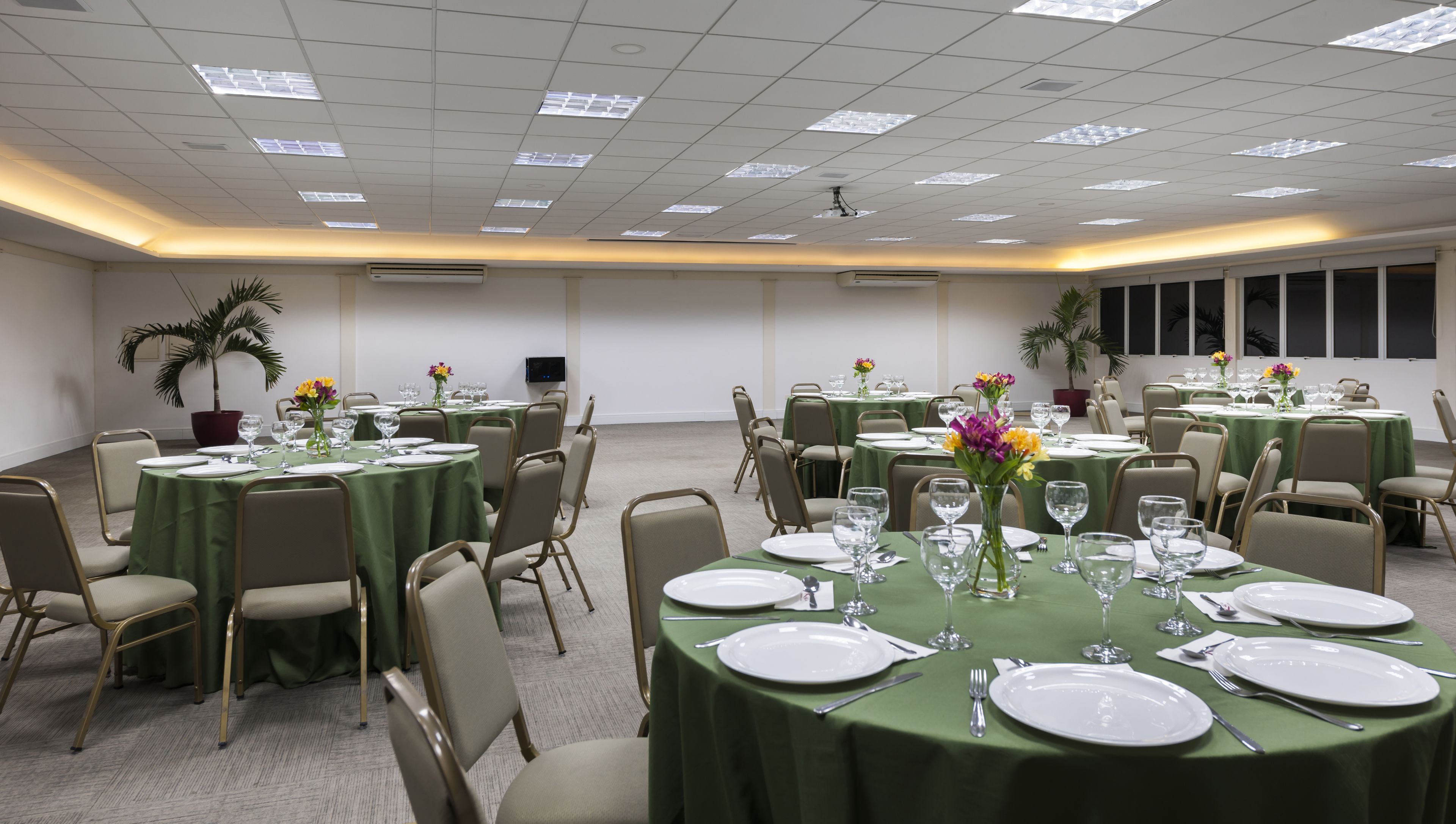 Un salón de conferencias con mesas redondas, sillas y manteles verdes.