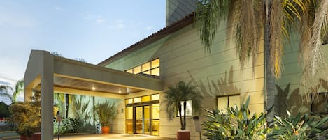 A modern building with a covered entrance, large windows, and potted plants.