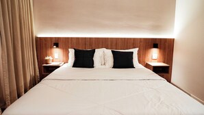 Una habitación de hotel con una cama grande, dos mesitas de noche con lámparas y un cabecero de madera.