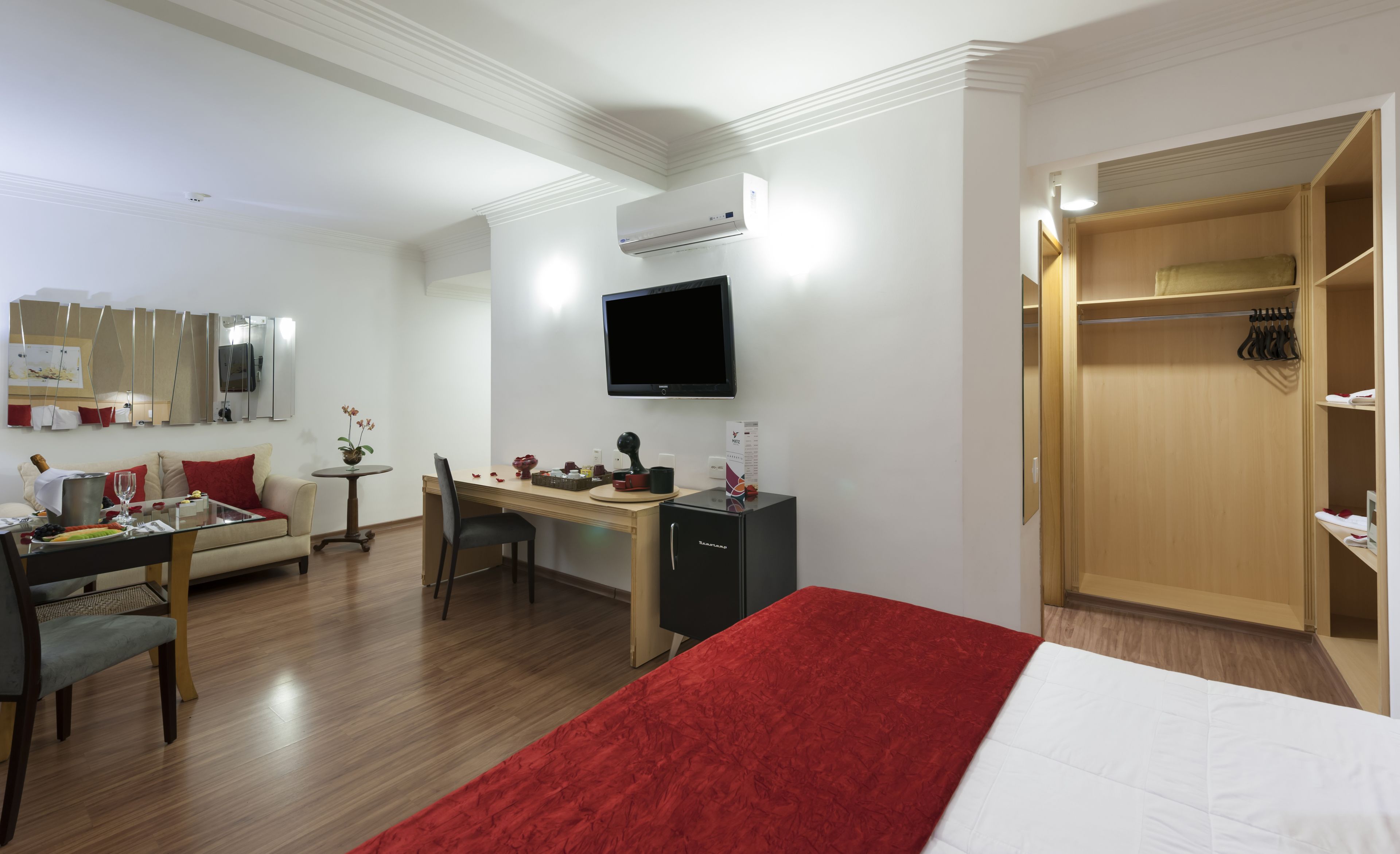 Habitación de hotel con cama, escritorio, silla, televisor, armario y una mesita con planta.
