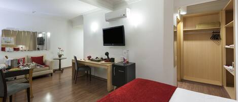 Habitación de hotel con cama, escritorio, silla, televisor, armario y una mesita con planta.