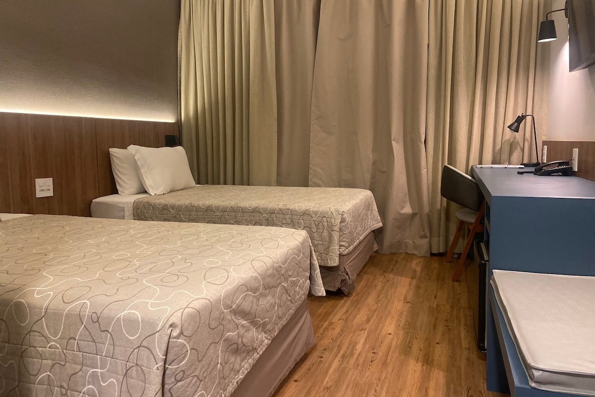 A hotel room with two beds, a desk, and a chair.