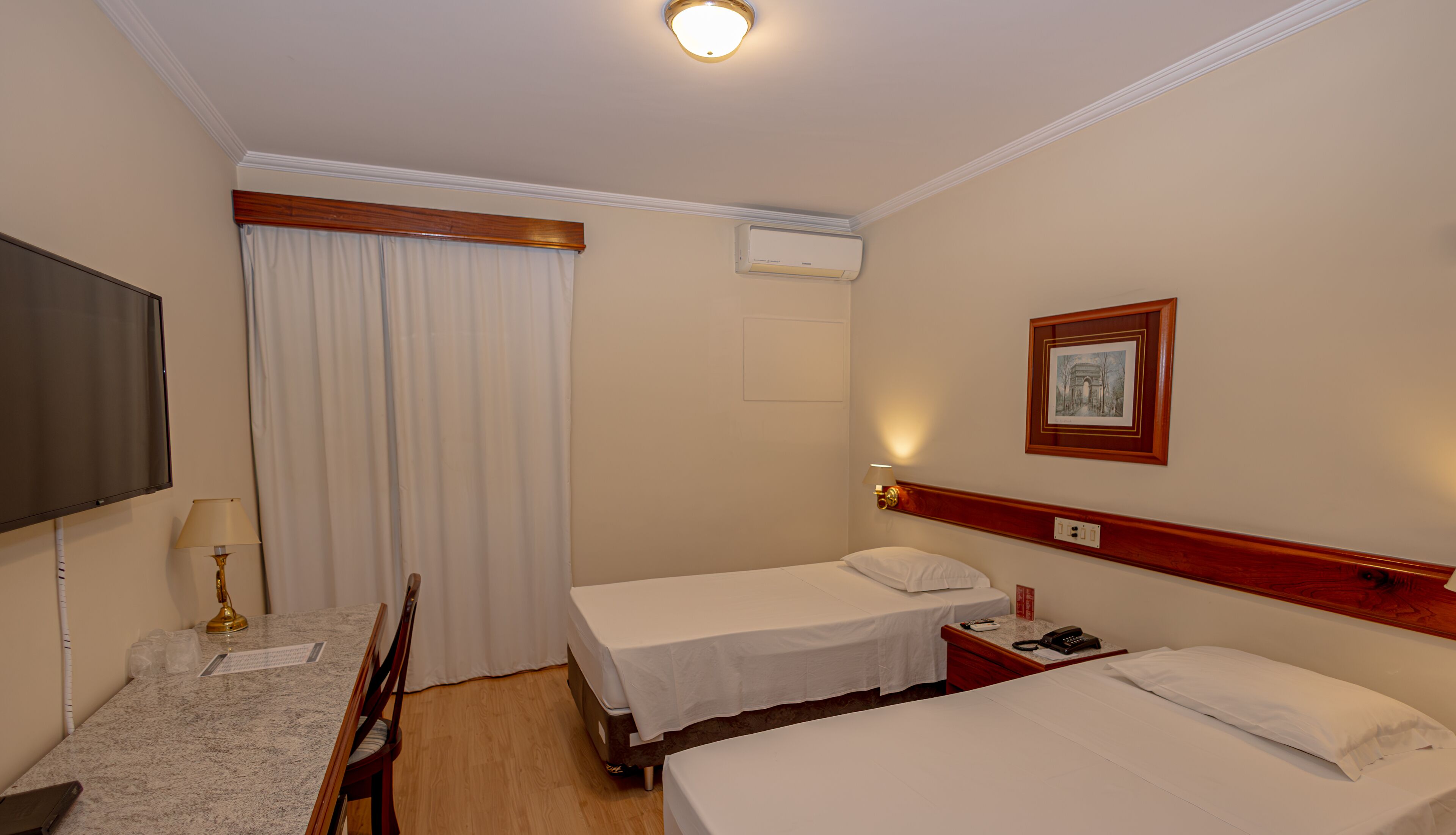 Habitación de hotel con dos camas, un escritorio con silla, un televisor y un cuadro en la pared.